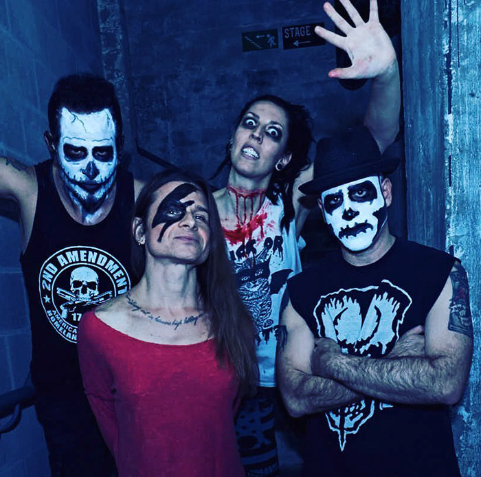 Rock singer with bandmates wearing face paint and dark clothing, posing in a dimly lit corridor.