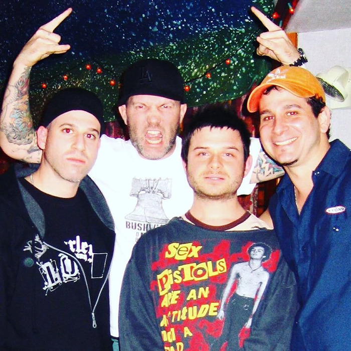 Rock singer with friends, wearing casual shirts and hats, posing energetically in a vibrant setting.