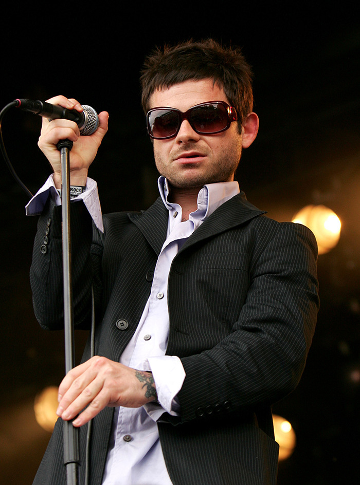 Rock singer performing on stage, wearing sunglasses and a pinstripe suit, holding a microphone.