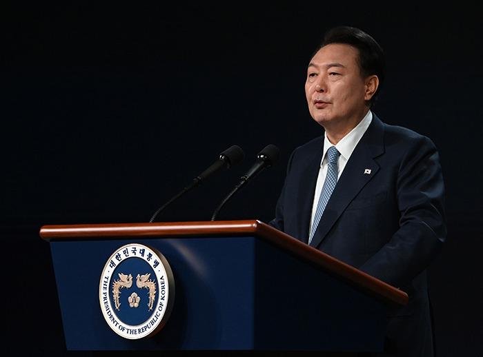 South Korea's president giving a speech, standing at a podium against a dark backdrop, related to martial law declaration.