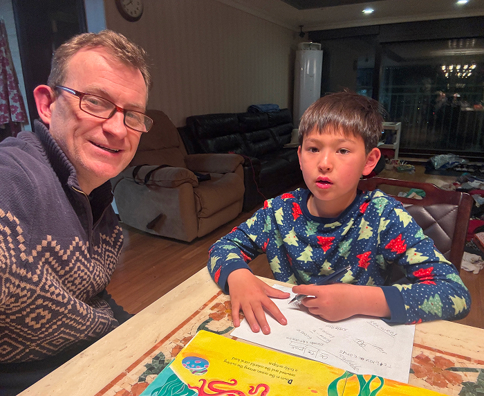 Man in glasses and a festive sweater with his son doing homework, reminiscent of viral "BBC Dad" moment.