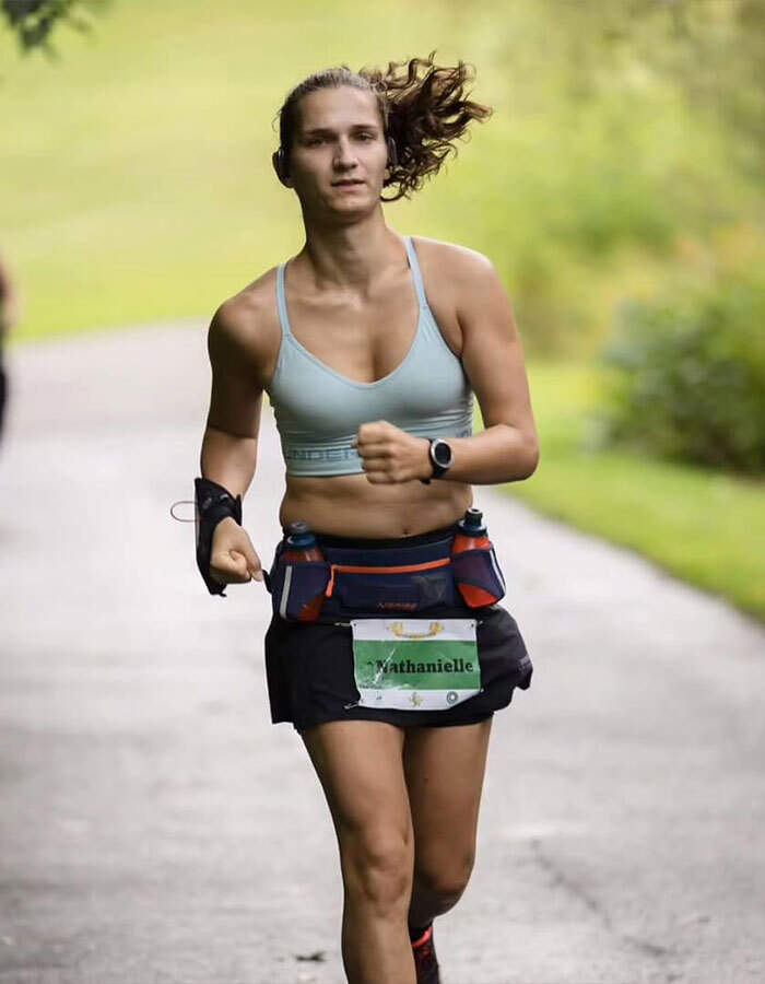Trans runner competing in a race, advocating for transgender inclusion in women's sports, running on a park trail.