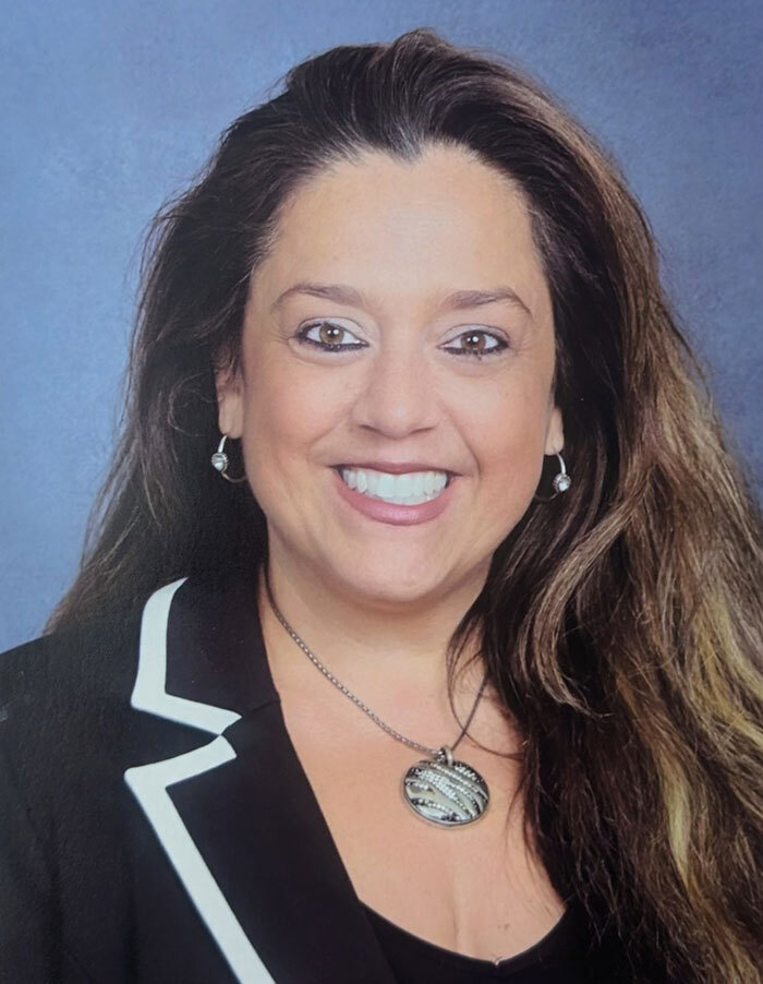 A smiling woman in professional attire, related to a school principal incident involving students drinking at her home.