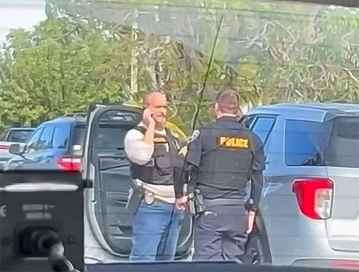 Police officers at a scene involving school principal arrest, outdoors near vehicles.