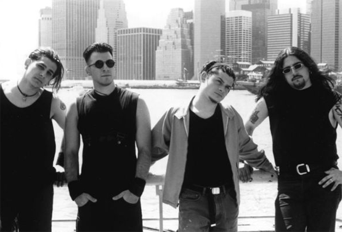 Rock singer with three band members posing against city skyline.