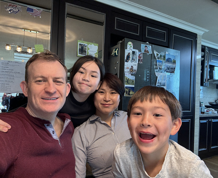 Family of "BBC Dad" with children grown up, smiling in the kitchen.