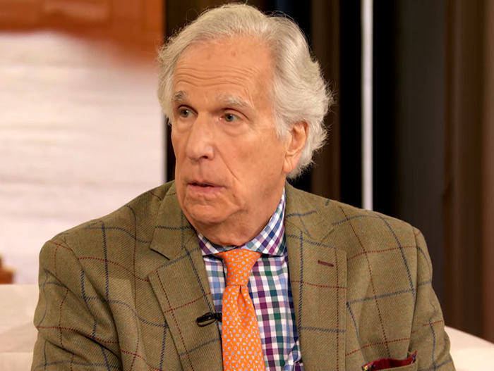 Henry Winkler in a checkered shirt and plaid jacket discussing LA wildfires theory.