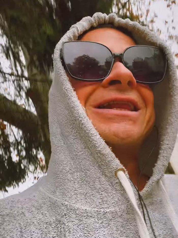 Rock singer in sunglasses and hoodie outdoors, discussing detransition plans.