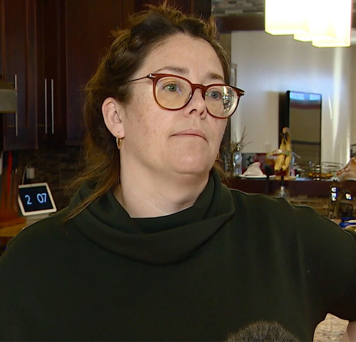 Woman in glasses discussing a family-held-hostage incident at a Cancun resort, wearing a dark sweater indoors.