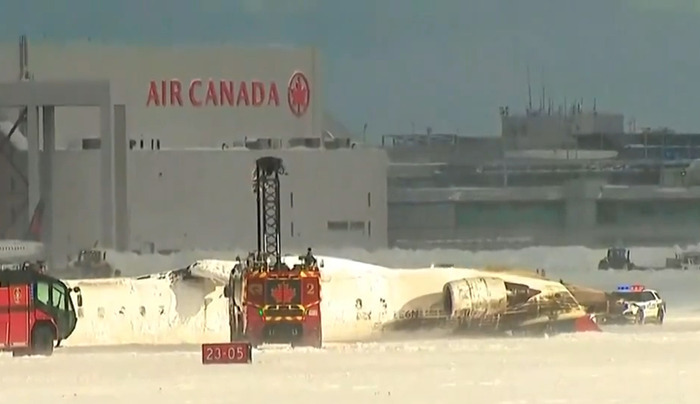 Delta Airlines plane flipped upside down post-crash landing, emergency vehicles present.