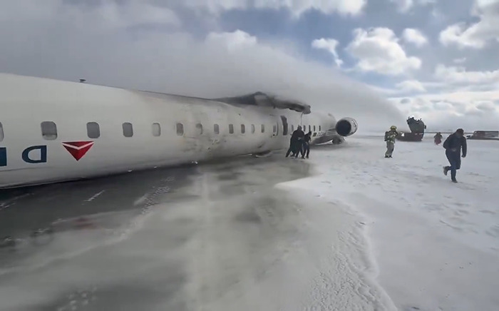 Delta Airlines plane upside down after crash landing on icy terrain, surrounded by rescue personnel.