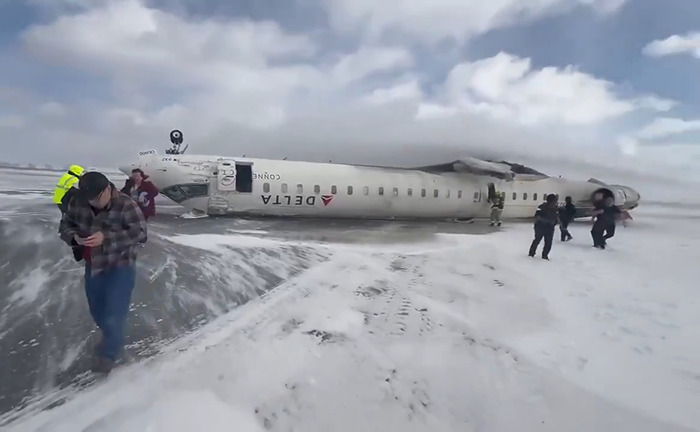 Delta Airlines plane flipped upside down on snowy ground after crash landing, passengers and crew nearby.