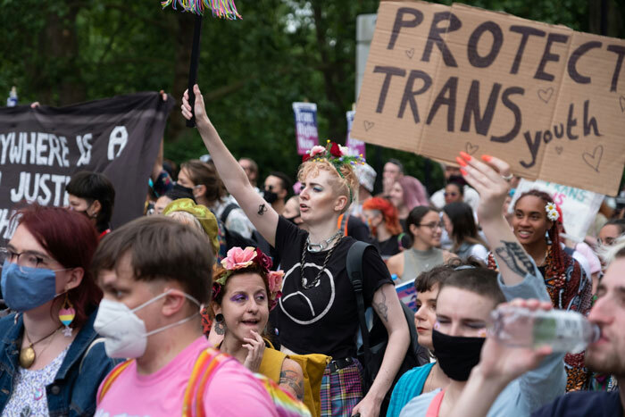 Protesters advocate for transgender inclusion in sports, holding signs supporting trans youth during a rally.