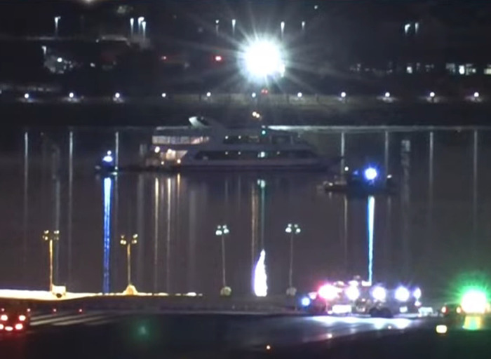 Emergency vehicles and a boat at night reflecting on water after DC American Airlines plane crash.