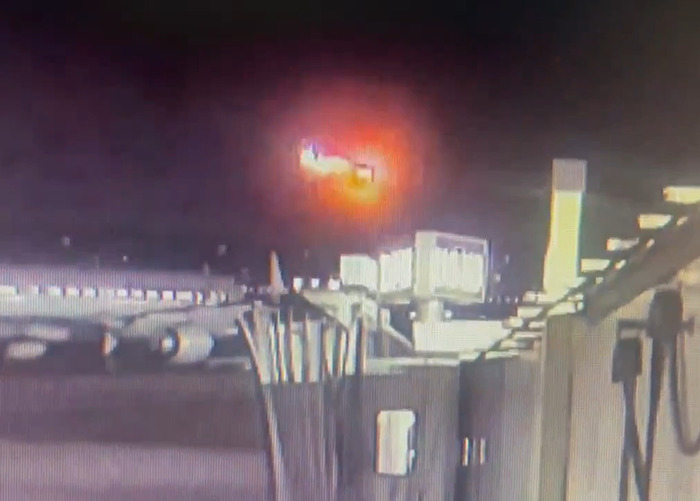 Blurry image of DC American Airlines plane crash at night, with bright fireball in the sky.