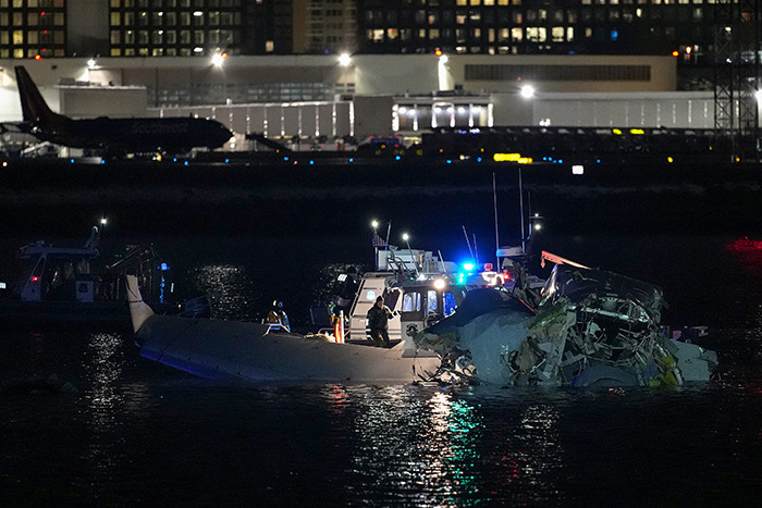 Boat crews inspect wreckage in water at night after plane crash near DC.