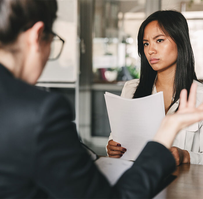 Woman in job interview looking upset, holding documents, after being asked a relationship question by CEO.