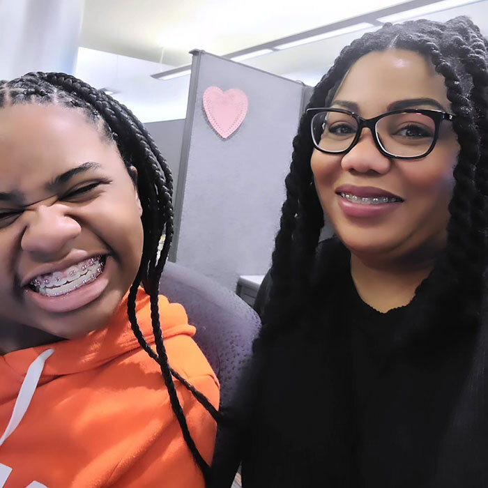 Kelaia Turner in an orange hoodie, mom Ty Turner in glasses, in an office setting with a heart decoration on the wall.