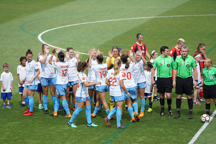 Women&rsquo;s football team on the field celebrating before a match, with referees standing nearby.