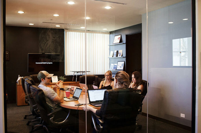 People in a modern office meeting room, discussing around a table with laptops.