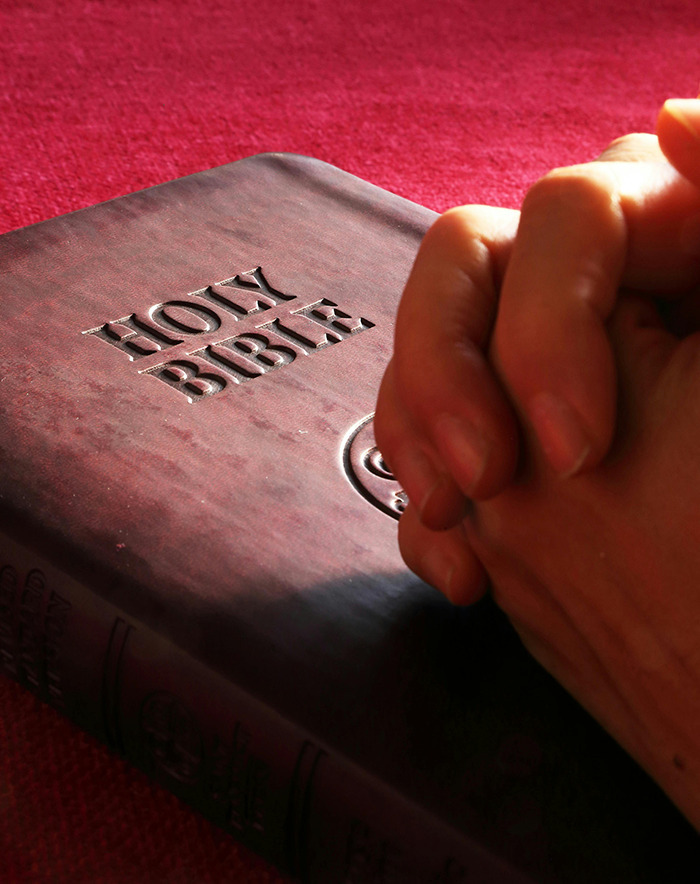 Hands clasped in prayer on a Bible, symbolizing Christian themes during a Christmas billboard debate.