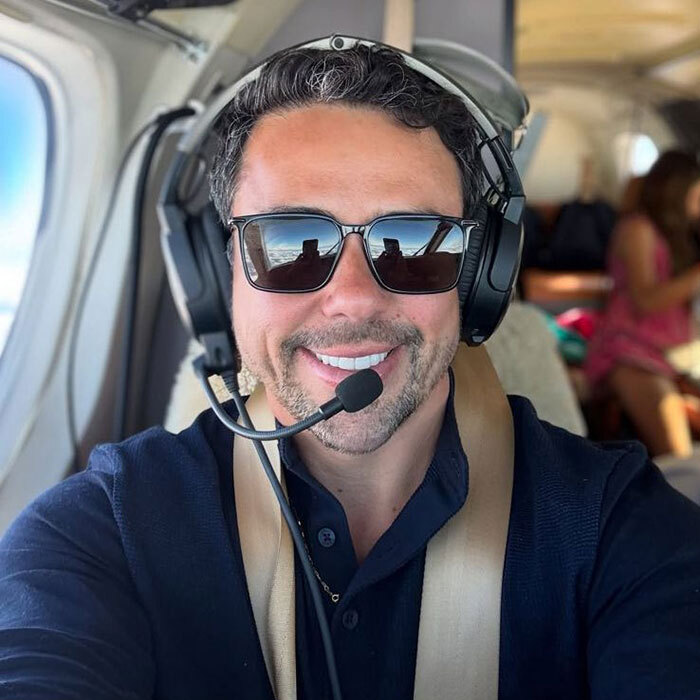 Pilot in cockpit smiling, wearing sunglasses and headset, involved in the latest aviation disaster.