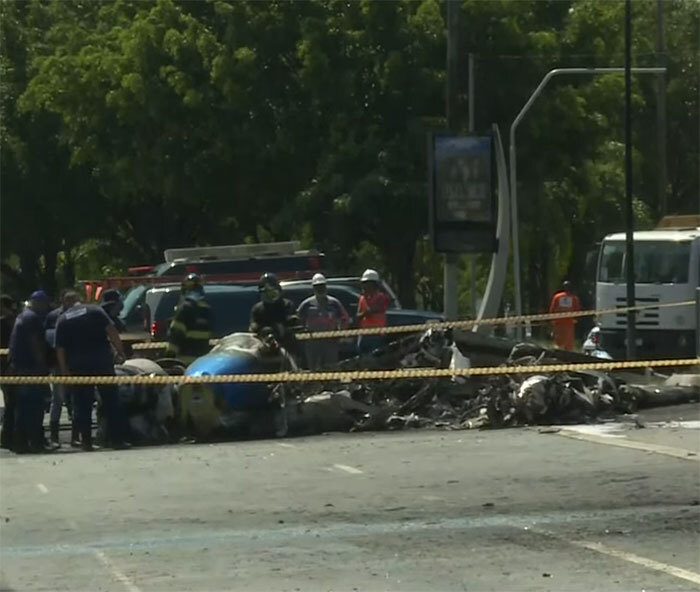Aviation disaster scene with plane wreckage and emergency responders behind caution tape.