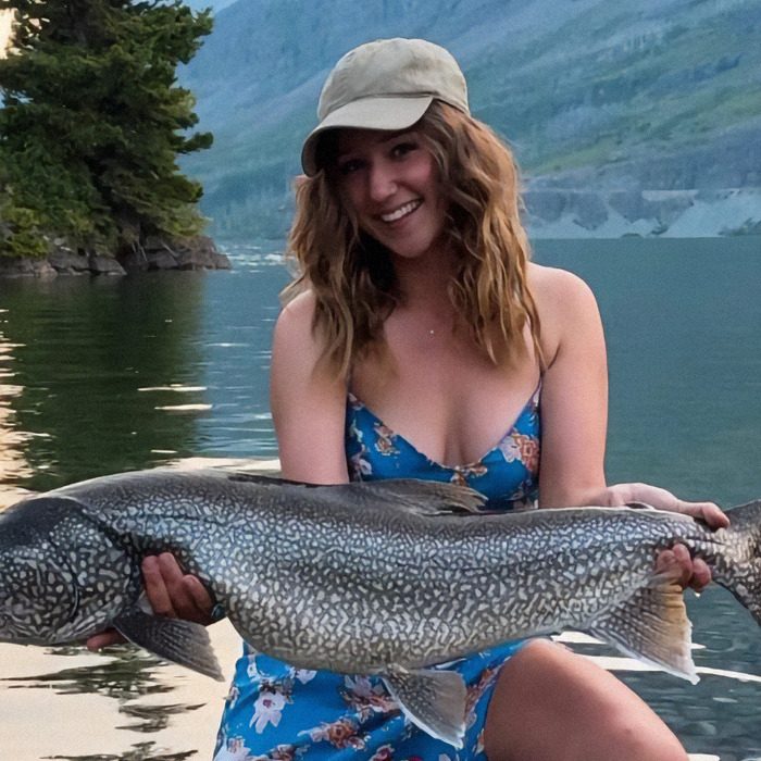 Woman in a floral dress holding a large fish by a lake, smiling; related to American tourist and baby wombat incident.