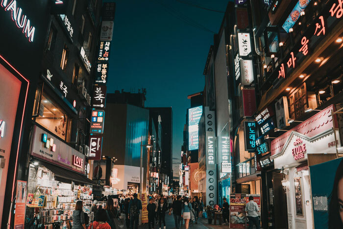 A bustling South Korean street at night, with illuminated signs and a crowd of people, reflecting urban life.