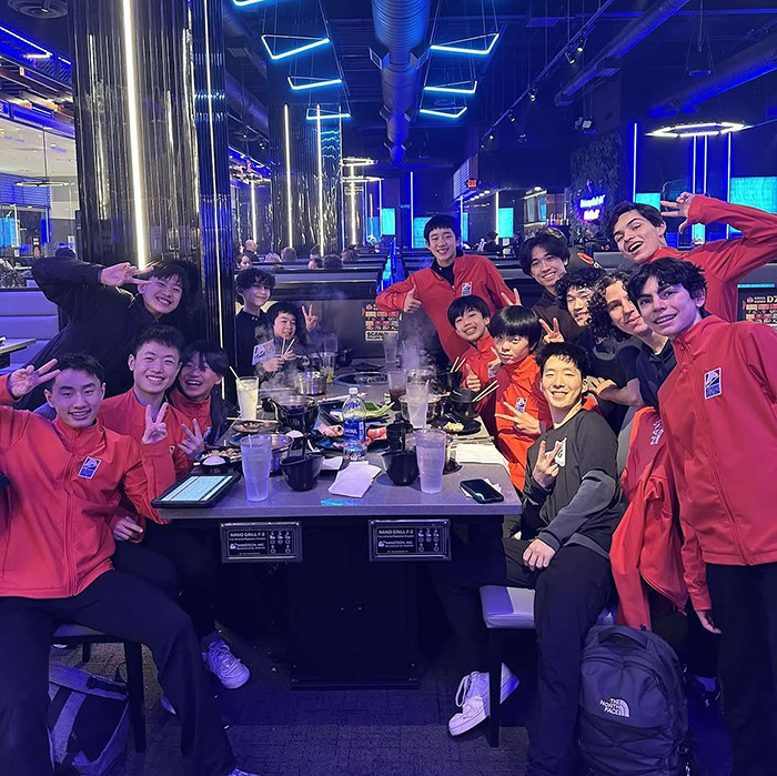 Teen skaters smiling at a restaurant, wearing red jackets, around a table with food and drinks.