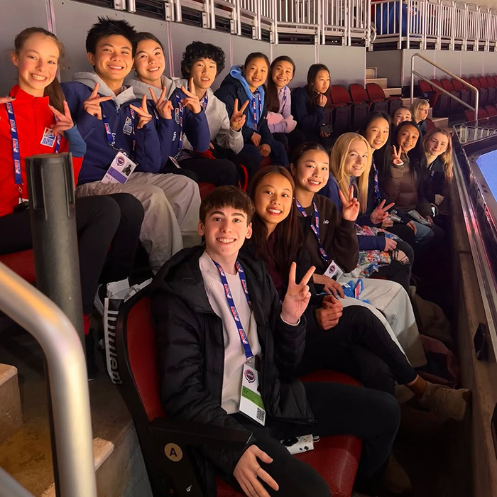 Teen skaters smile and hold peace signs in arena seats, capturing a joyful moment.