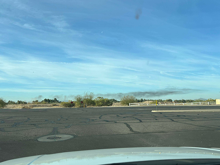 Smoke in Arizona sky after two planes collide mid-air, viewed from car windshield.