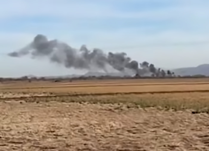 Smoke rising in Arizona field after two planes collide mid-air, with clear skies above.