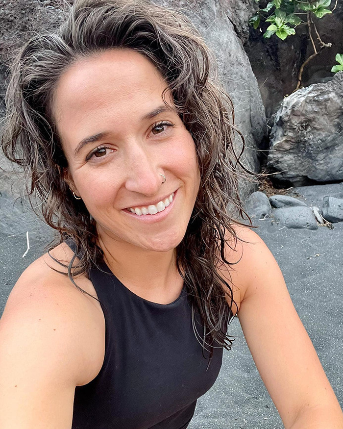 Britt Boril at a rocky beach, smiling for a selfie.