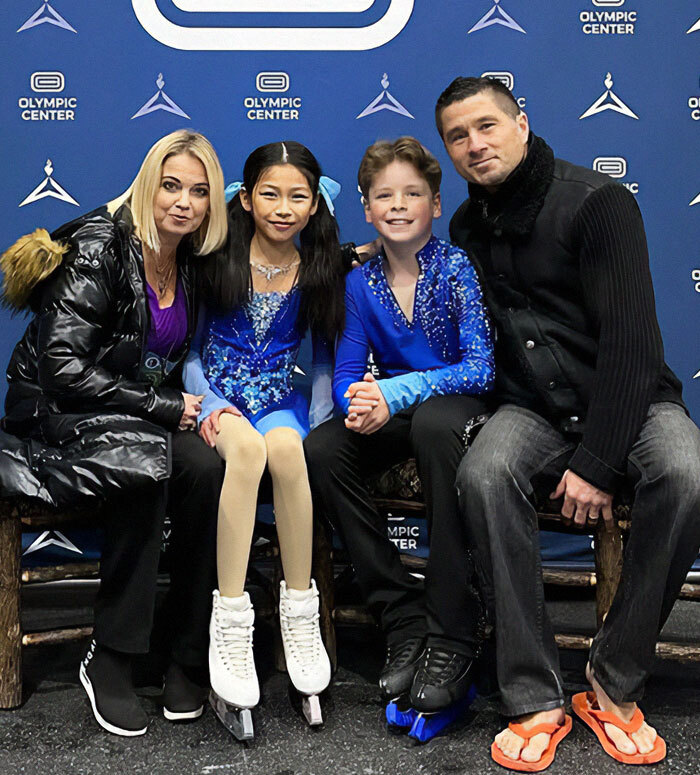 Adorable child ice skating duo with two adults at an Olympic Center event.