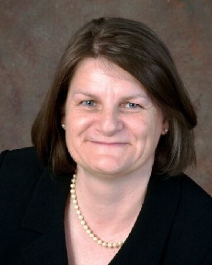 Middle-aged woman with short brown hair wearing a black blazer and pearl necklace, related to judge suspended for evading ICE agents.