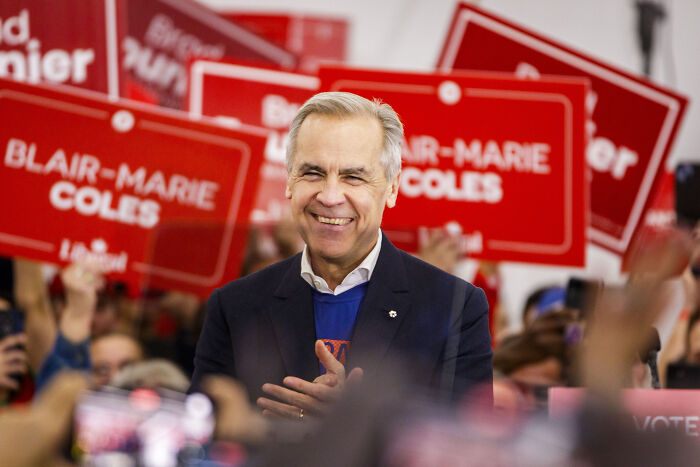 Smiling man in a crowd holding red signs during Canada election event.