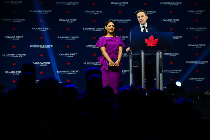 Mark Carney speaking at Canada election event, accompanied by a woman in a purple dress.