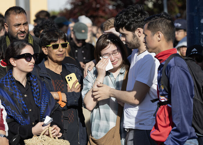 Individuals gathering somberly at a Vancouver festival after car-ramming attack, some comforting each other.