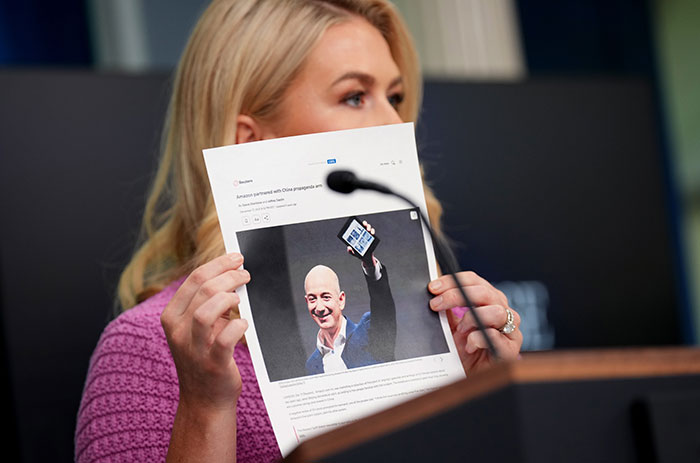 Woman holding printed photo of Jeff Bezos while speaking at a podium about Amazon delivery and job cuts discussion.