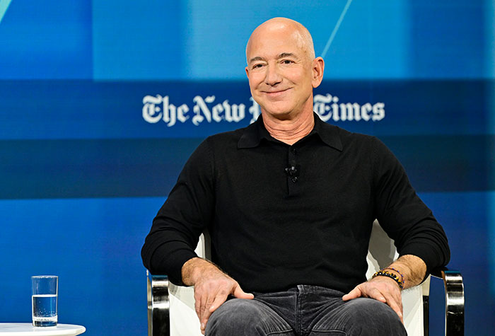 Jeff Bezos smiling in a black shirt during a New York Times event amid Amazon delivery and UPS job cuts discussion.