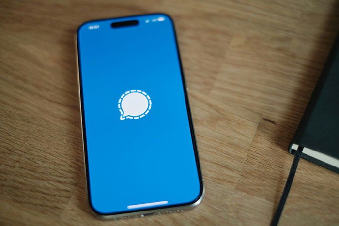 Smartphone displaying Signal app on a wooden table, related to Pete Hegseth and war plans discussion.