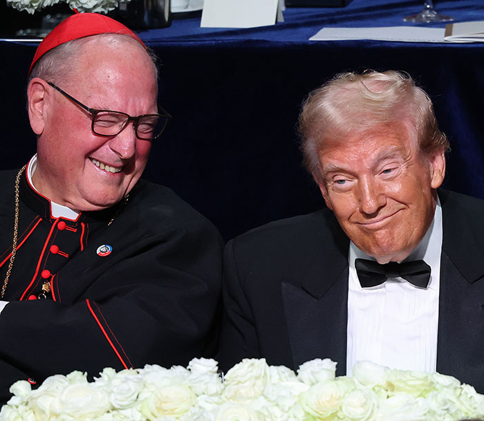 Donald Trump in a tuxedo sitting beside a cardinal at a formal event, smiling and sharing a light moment.