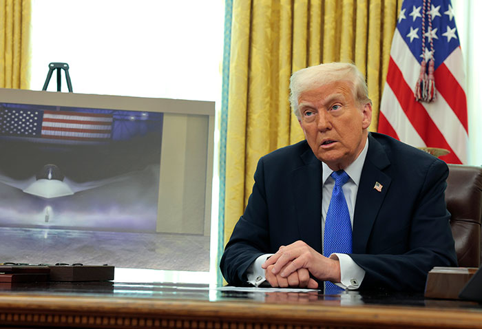 A man in a suit in an office with a jet photo, related to Russia, sanctions, and Boeing negotiations.