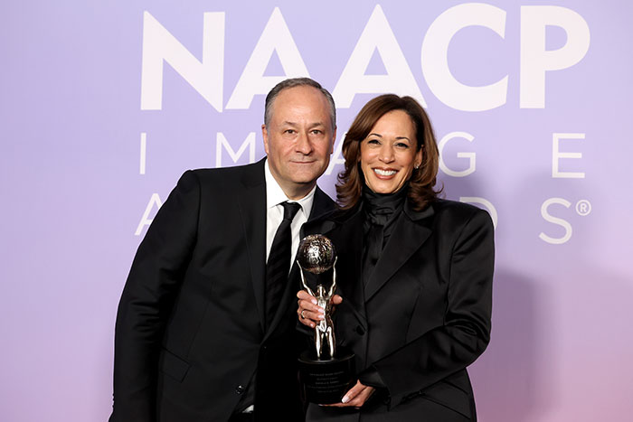 Kamala Harris and husband Doug Emhoff posing together at the NAACP Image Awards holding a trophy in formal black attire.