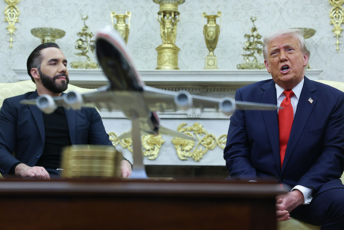 Two men seated near a model airplane in an ornate room, discussing a topic related to Home Alone 2 director's cameo concerns.