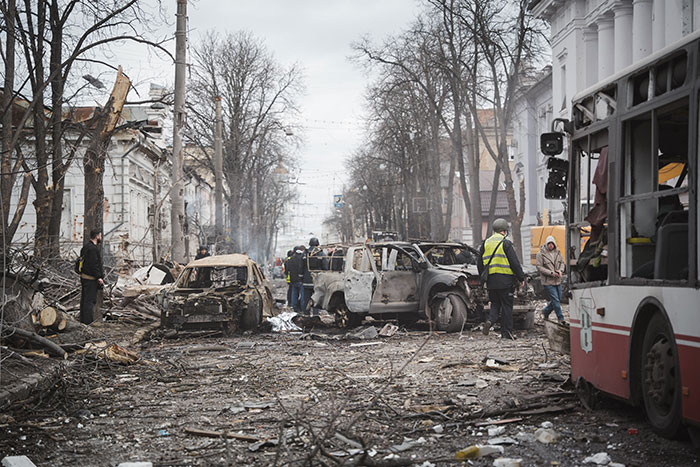 War-torn street in Ukraine with damaged vehicles and debris as NATO responds to ongoing strikes.