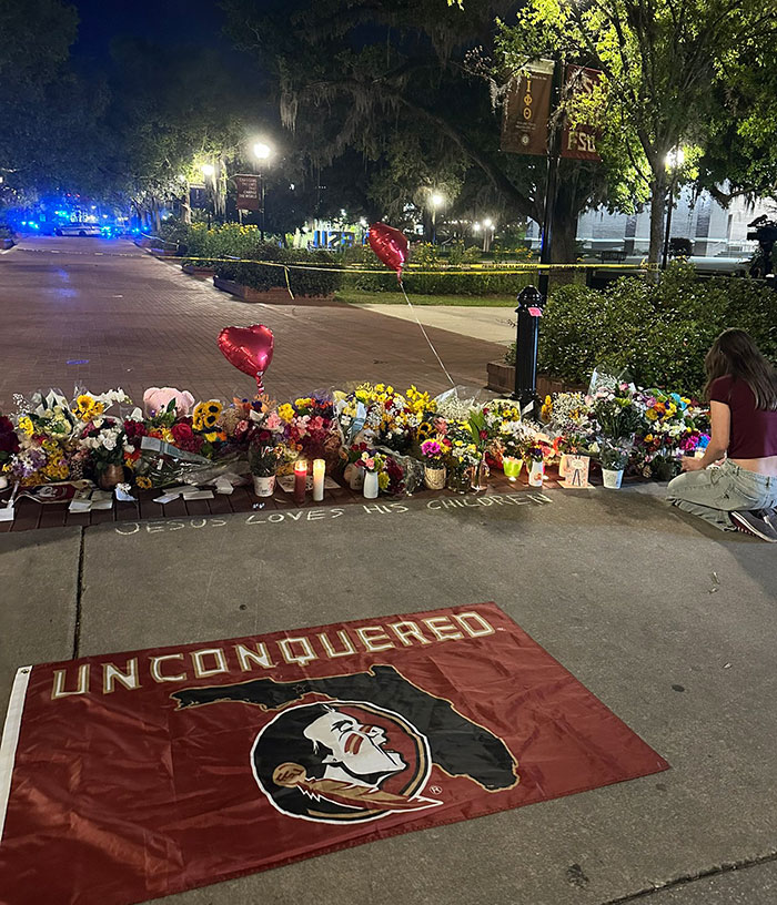 FSU memorial with flowers and candles honoring victims of campus shooting, featuring an "Unconquered" flag and tributes.