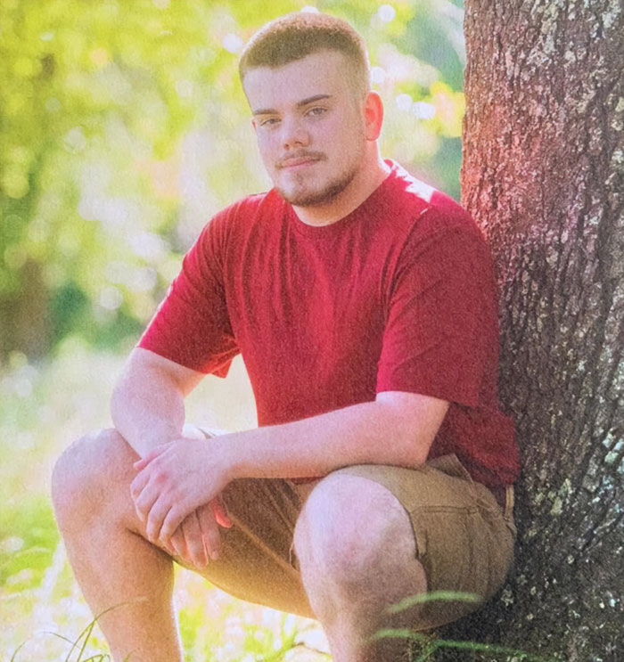 Man in a red shirt sitting by a tree in a sunny, grassy area, related to FSU shooter events.