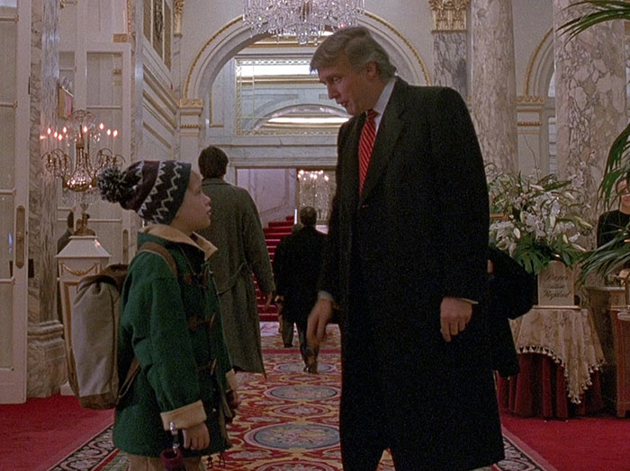 Child actor and hotel guest in an ornate lobby scene from "Home Alone 2," featuring a famous cameo moment.